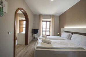 Una habitación de hotel con dos camas, televisión, escritorio y ventana con cortinas.