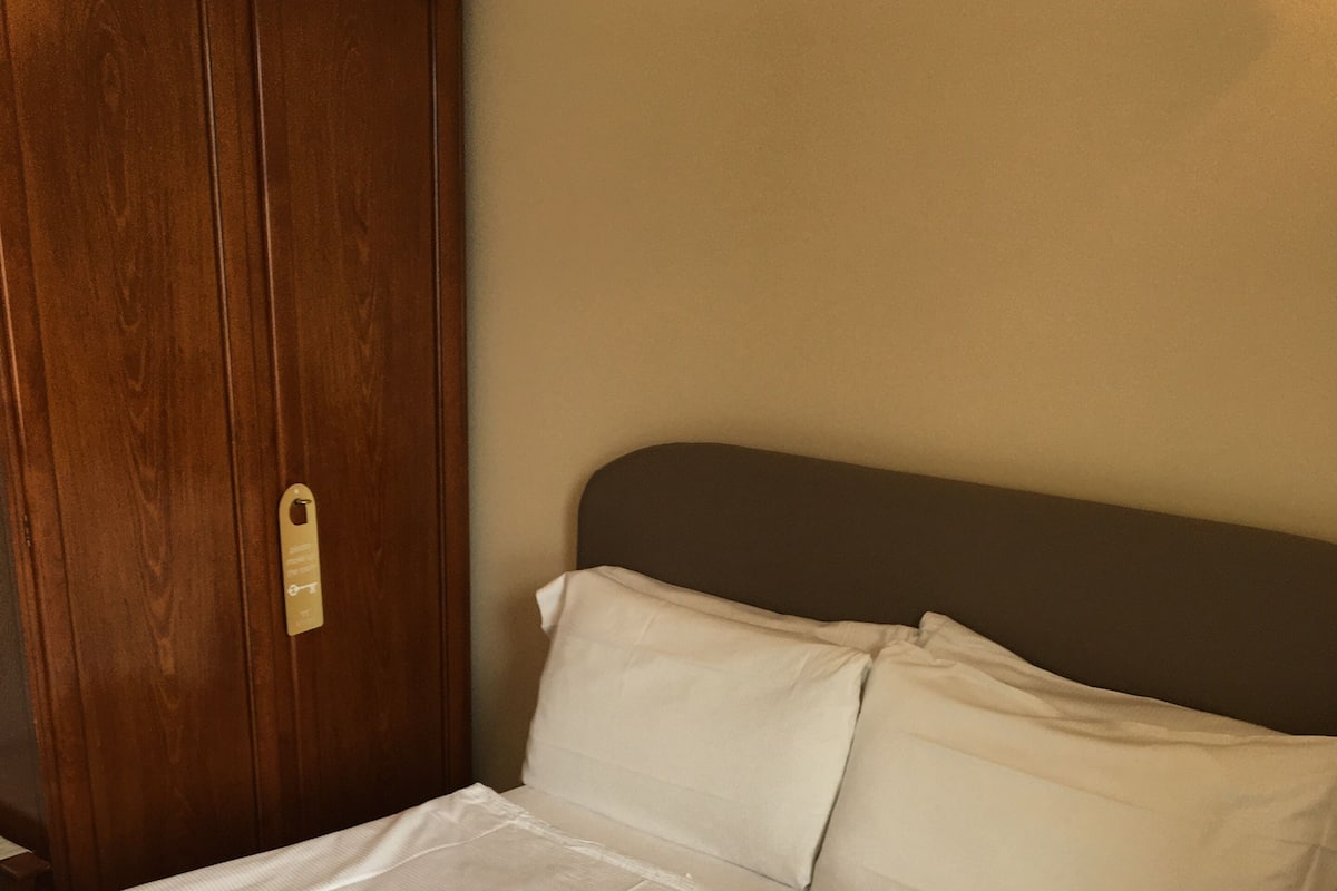 Un lit bien fait, avec du linge de lit blanc, une armoire en bois et une table de chevet avec une lampe.