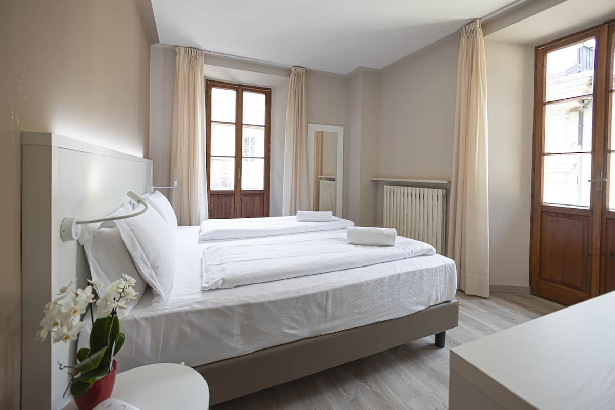 Une chambre à coucher avec un grand lit, une table de chevet avec une lampe, une fenêtre avec des rideaux et un radiateur.