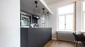 A modern bar area with a dark counter, wooden flooring, and geometric pendant lighting. - LVG Hotel Collection - Il Portico (Cannobio)