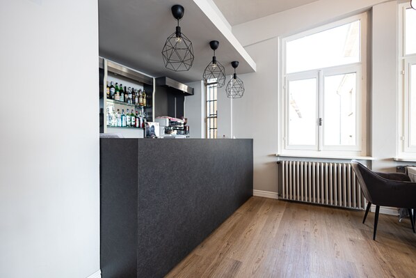 A modern bar area with a dark counter, wooden flooring, and geometric pendant lighting. - LVG Hotel Collection - Il Portico (Cannobio)