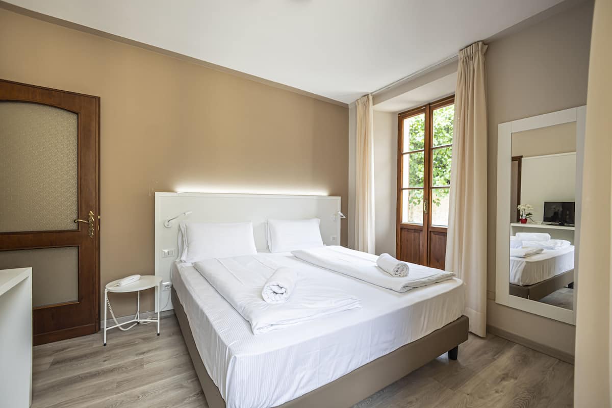 Une chambre à coucher avec un grand lit, une table de chevet, un miroir et une fenêtre avec des rideaux.