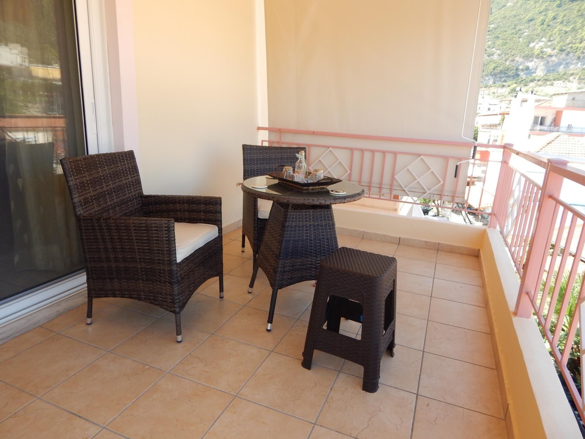 A balcony with wicker furniture, a small table, and a view of buildings and greenery.