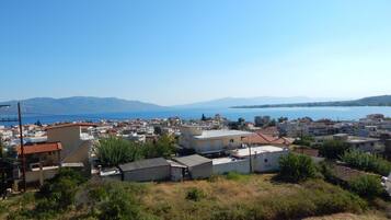 A coastal town with buildings, a clear sky, and a view of the sea and mountains in the distance.