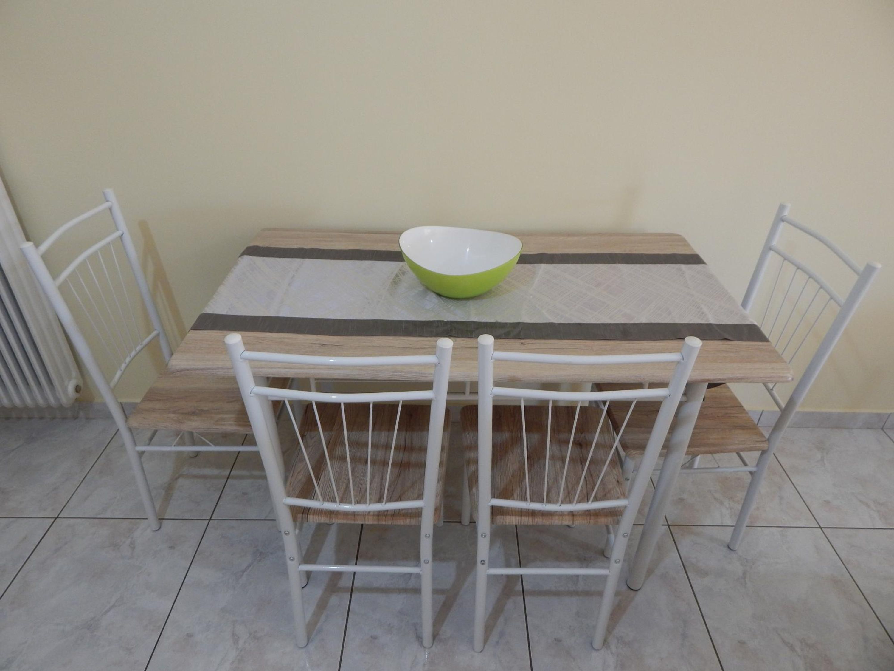 A dining table with a green bowl, four white chairs, and a striped table runner.