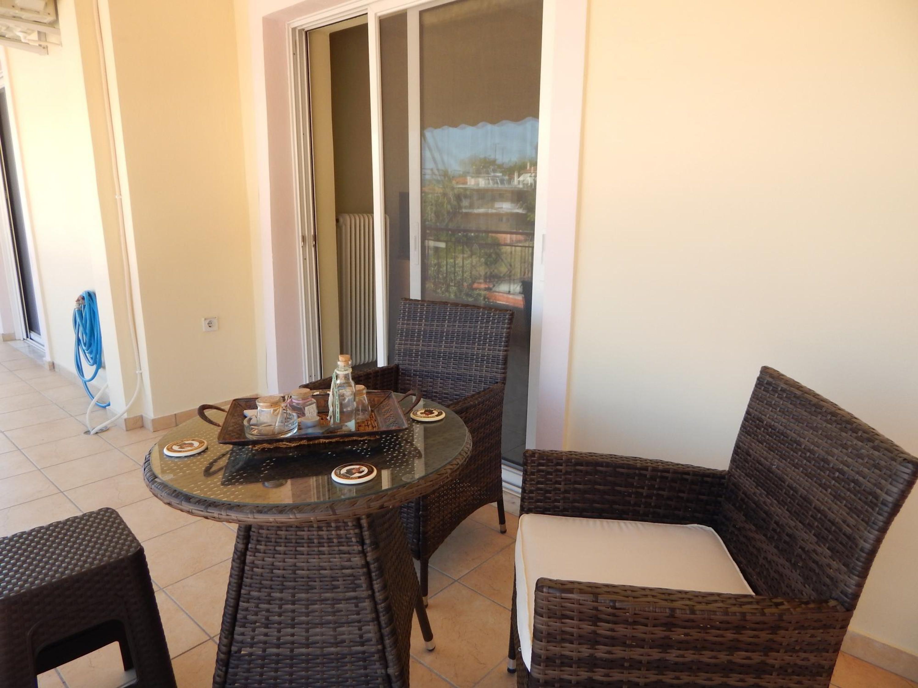 A balcony with wicker furniture, a glass table, and a view of a cityscape.