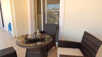 A balcony with wicker furniture, a glass table, and a view of a cityscape.