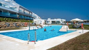 A swimming pool with people swimming and relaxing, surrounded by modern buildings and a clear blue sky. - Via Celere 2405 Beautiful apartment with seaview (Casares)