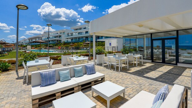 An outdoor patio area with white furniture, a pool, and a modern building in the background. - Via Celere 2405 Beautiful apartment with seaview (Casares)