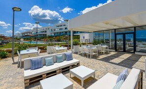 An outdoor patio area with white furniture, a pool, and a modern building in the background. - Via Celere 2405 Beautiful apartment with seaview (Casares)