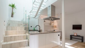 A modern kitchen with a central island, a glass staircase, and a flat-screen TV. - Estropada 1, detached apartment in Pedregalejo, Malaga, with sea views (Málaga)