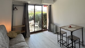 Un salon moderne comprenant un canapé, une table à manger avec deux chaises et une porte-fenêtre coulissante donnant sur un espace extérieur.