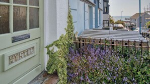 Een charmant herenhuis met een groene deur waarop 'MYRTLE' staat, een houten hek en een tuin vol paarse bloemen.