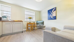 Una cocina moderna con armarios blancos, un comedor con mesa y sillas de madera, un televisor y un cuadro en la pared.