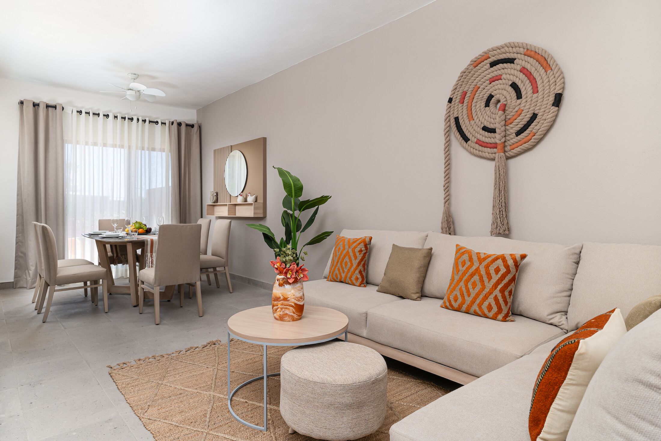 Una sala de estar moderna con un sofá color beige, una mesa redonda de centro y un comedor con sillas y una mesa.