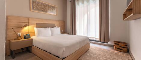 A neatly arranged bedroom with a wooden bed, bedside table with a lamp, a wall-mounted air conditioner, and a window with curtains.