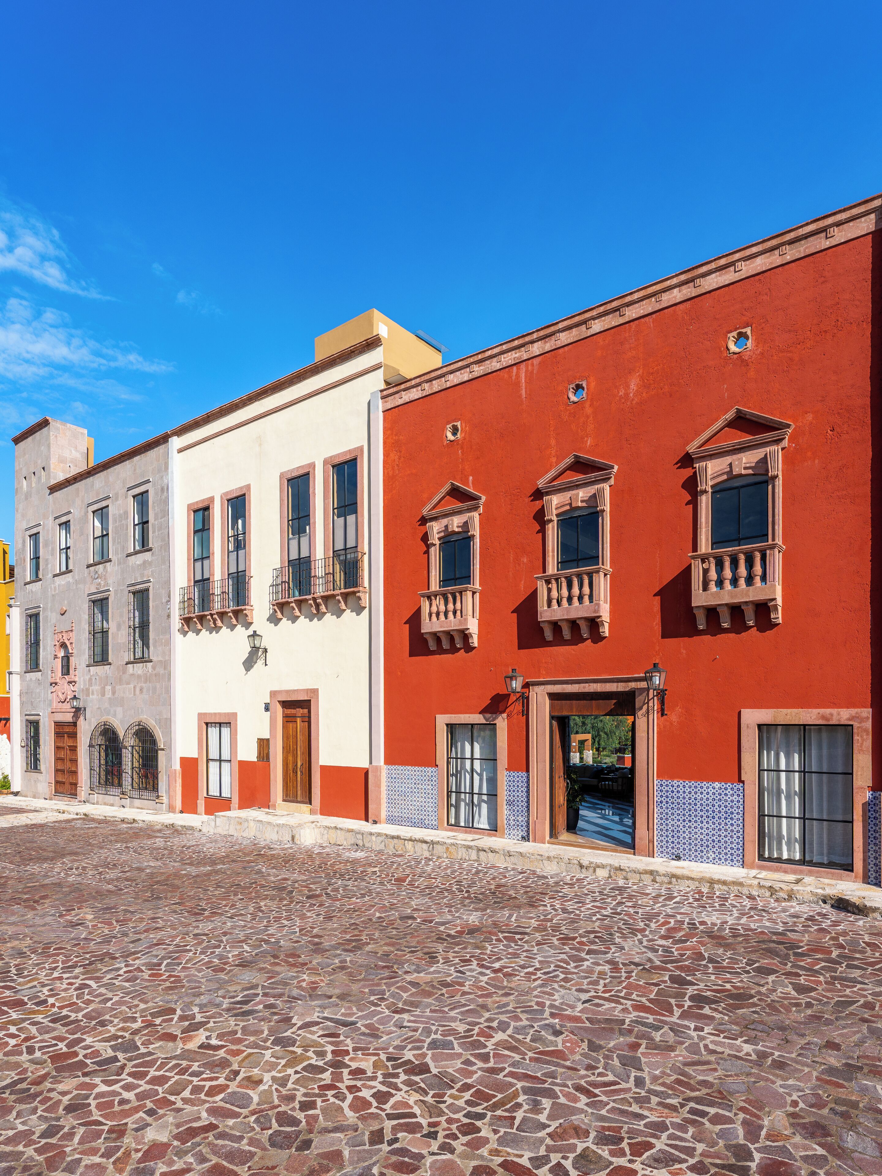 A cobblestone street with buildings featuring traditional architecture and a red facade.