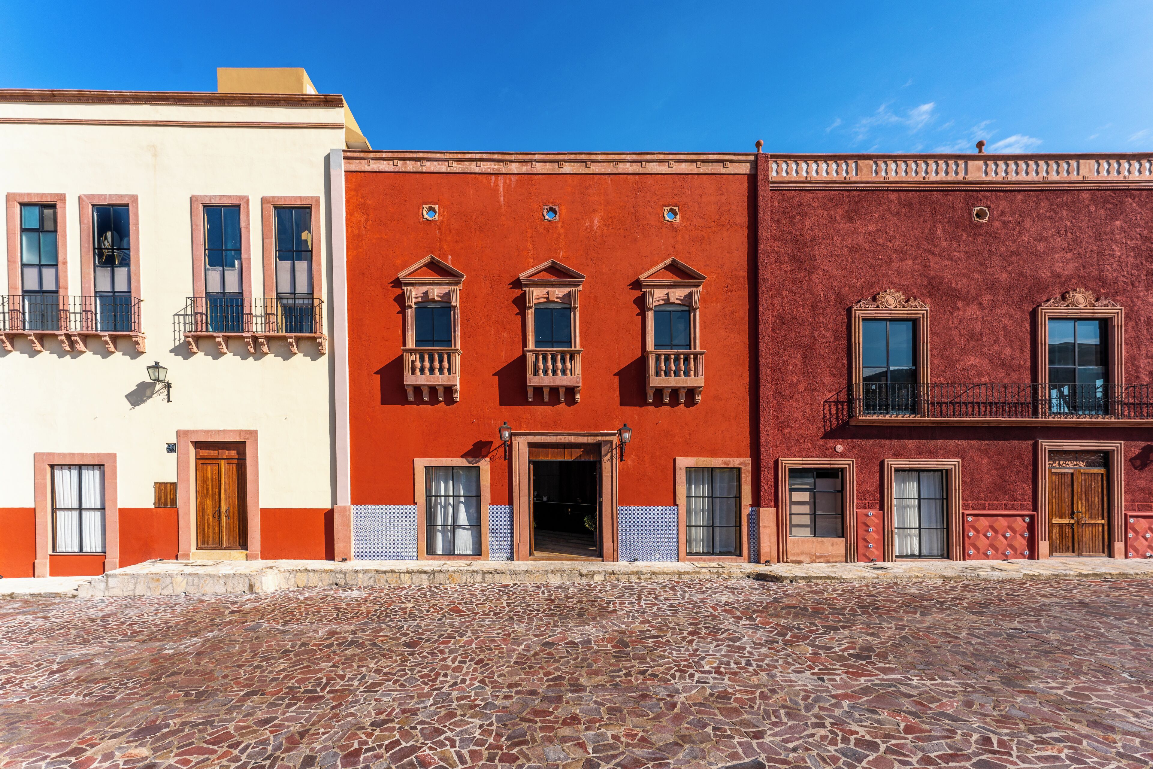 Eine Straße mit drei Gebäuden, jedes mit unterschiedlichem Architekturstil und Balkonen.