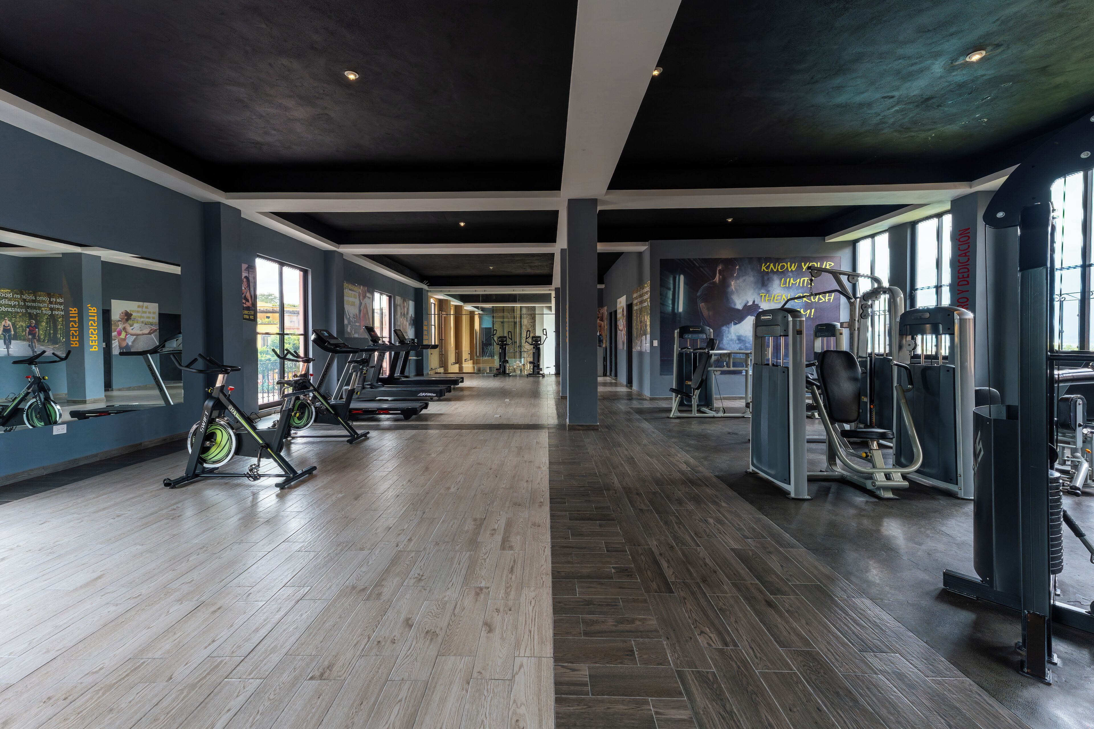 A gym with exercise equipment, wooden flooring, and large windows.
