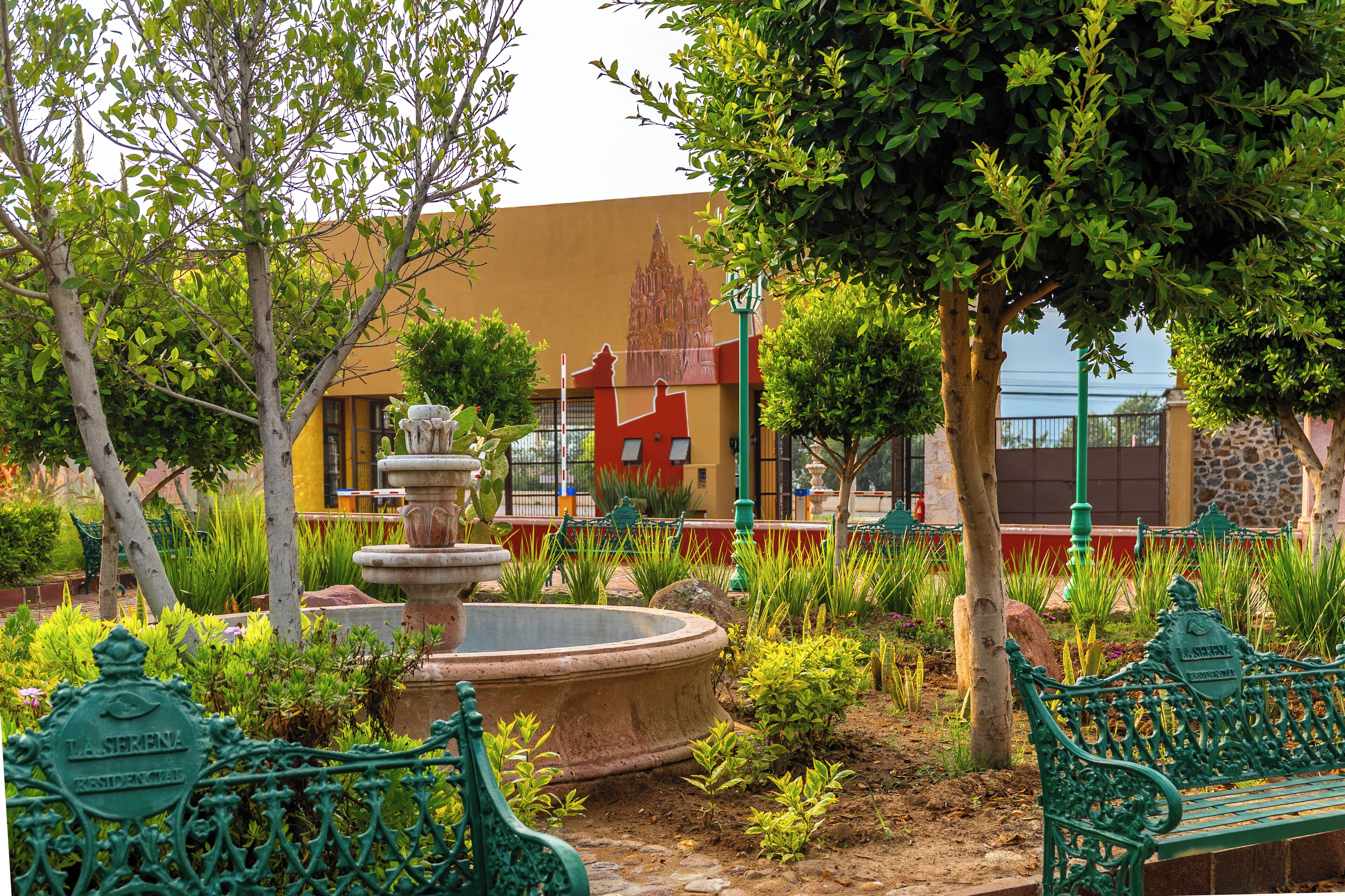 A garden with a fountain, benches, and a building with a mural.