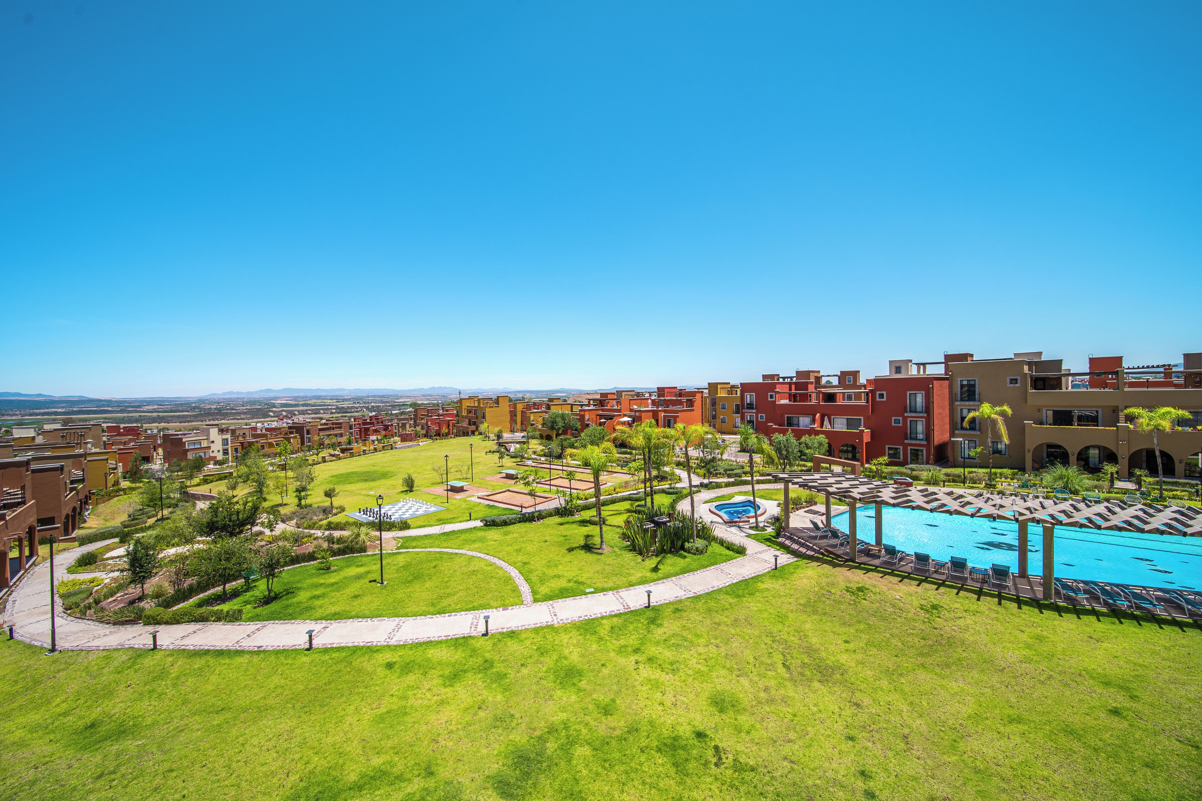 A residential area with a swimming pool surrounded by greenery and a clear blue sky.