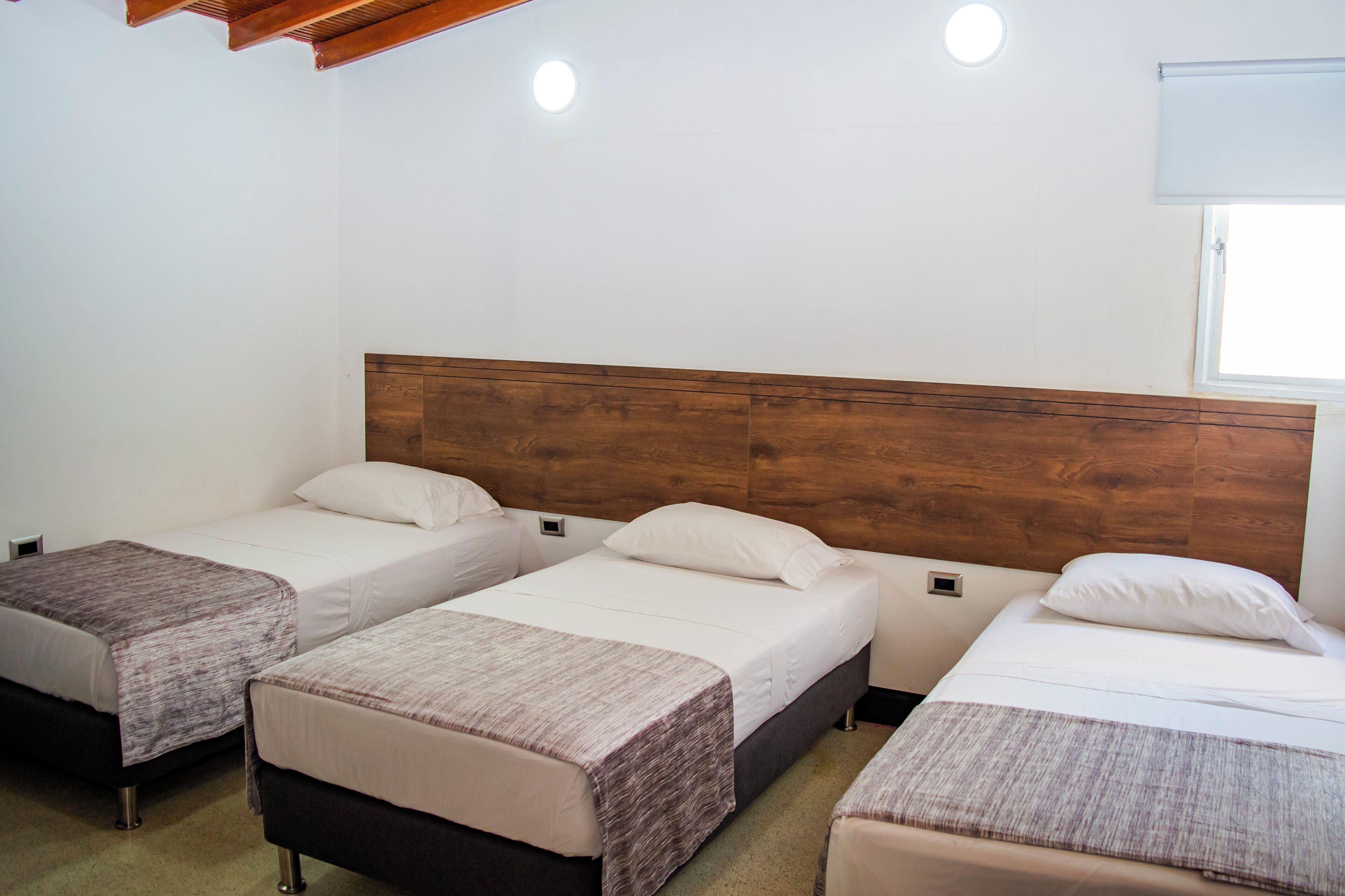 Habitación de hotel con tres camas individuales, cabeceros de madera y un ventanal con vistas.