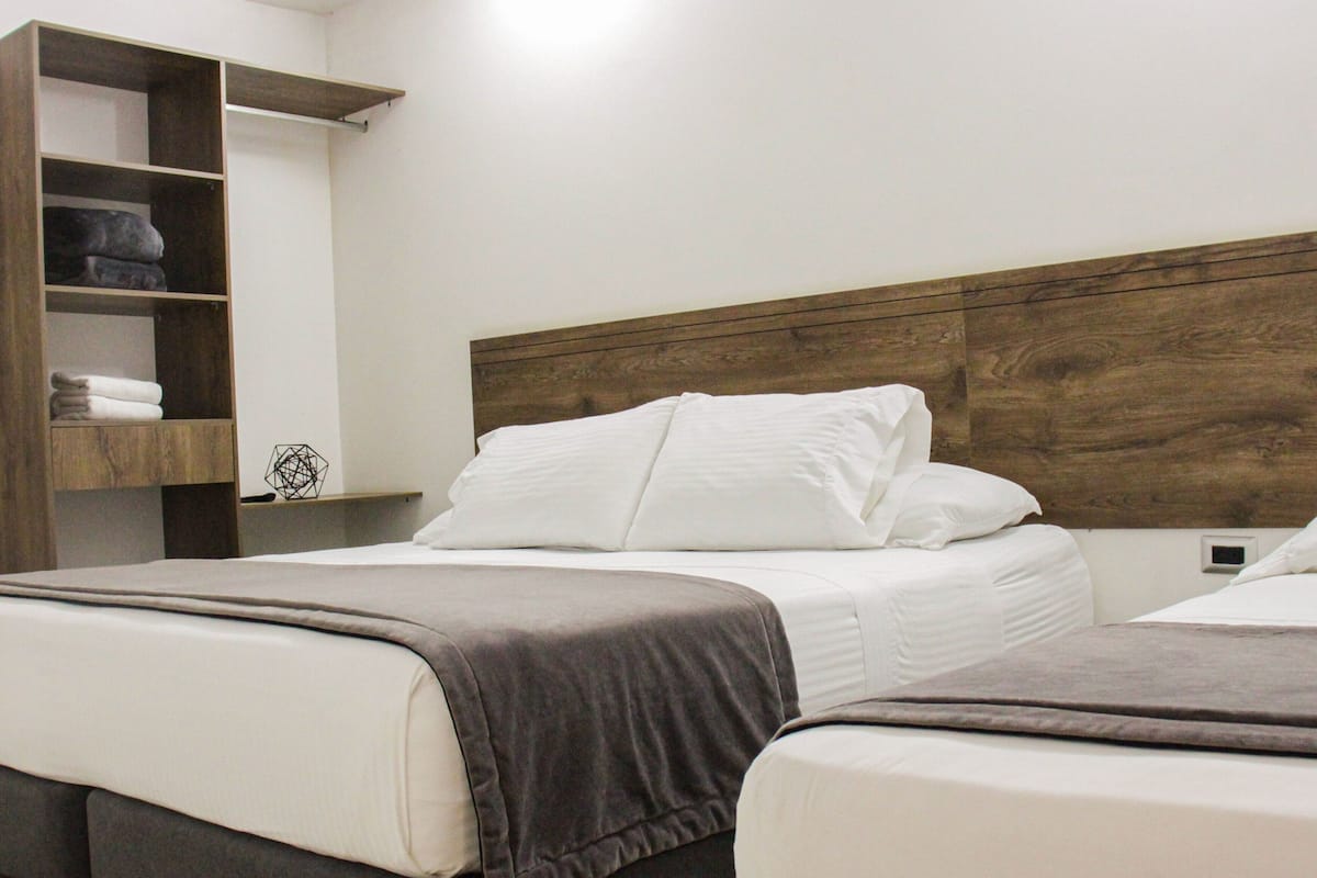 Ein Hotelzimmer mit zwei Betten, einem hölzernen Kopfteil und einer eingebauten Ablage mit gefalteten Handtüchern.