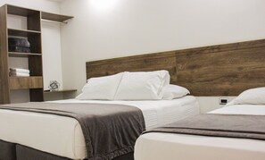 A hotel room with two beds, a wooden headboard, and a built-in shelf with folded towels. - Hotel Boutique Estadio Medellin (Medellín)
