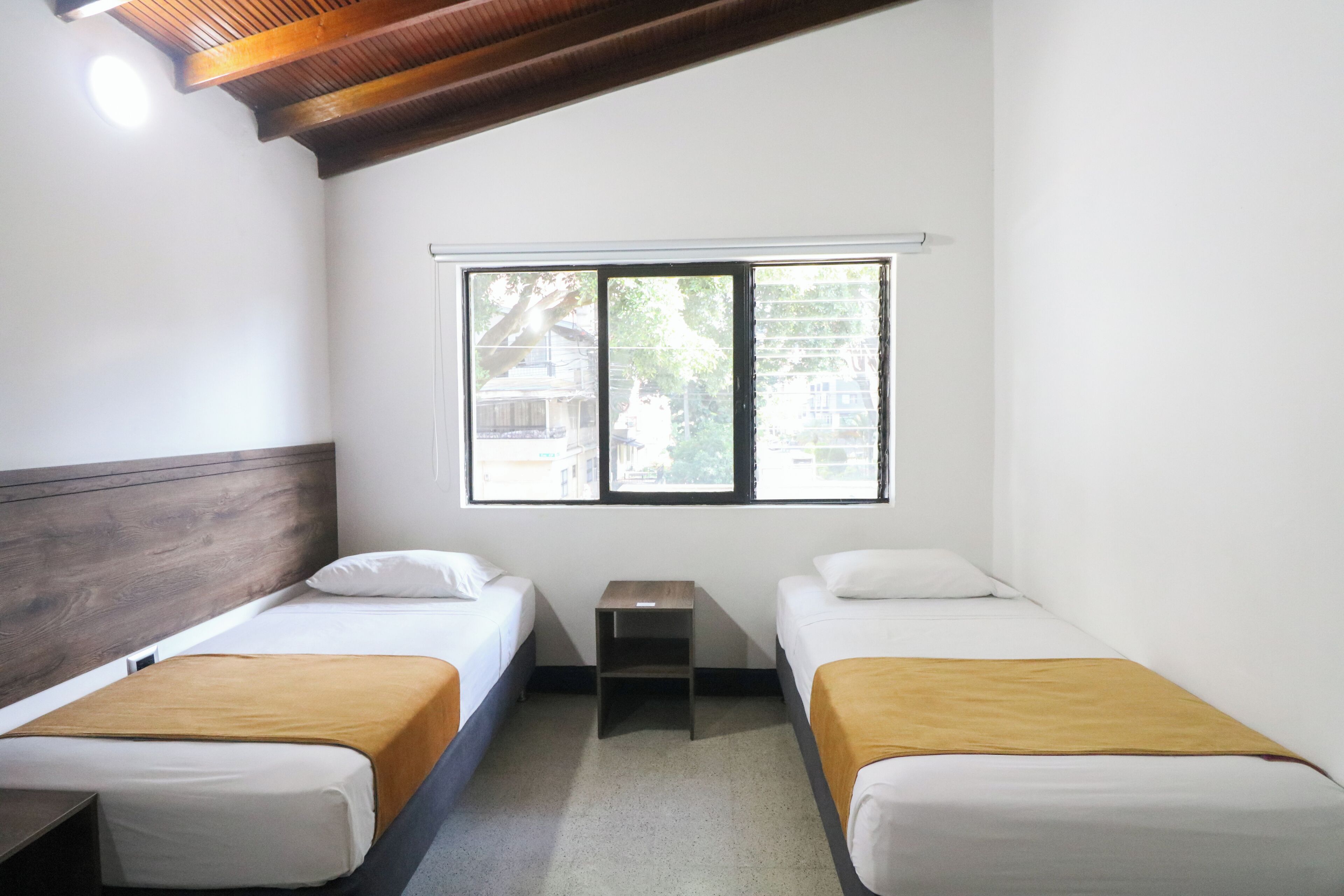 Una habitación con dos camas, una mesita y un ventanal.