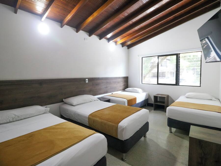 Quarto de hotel com três camas, vigas de madeira no teto, televisão e janela com vista.