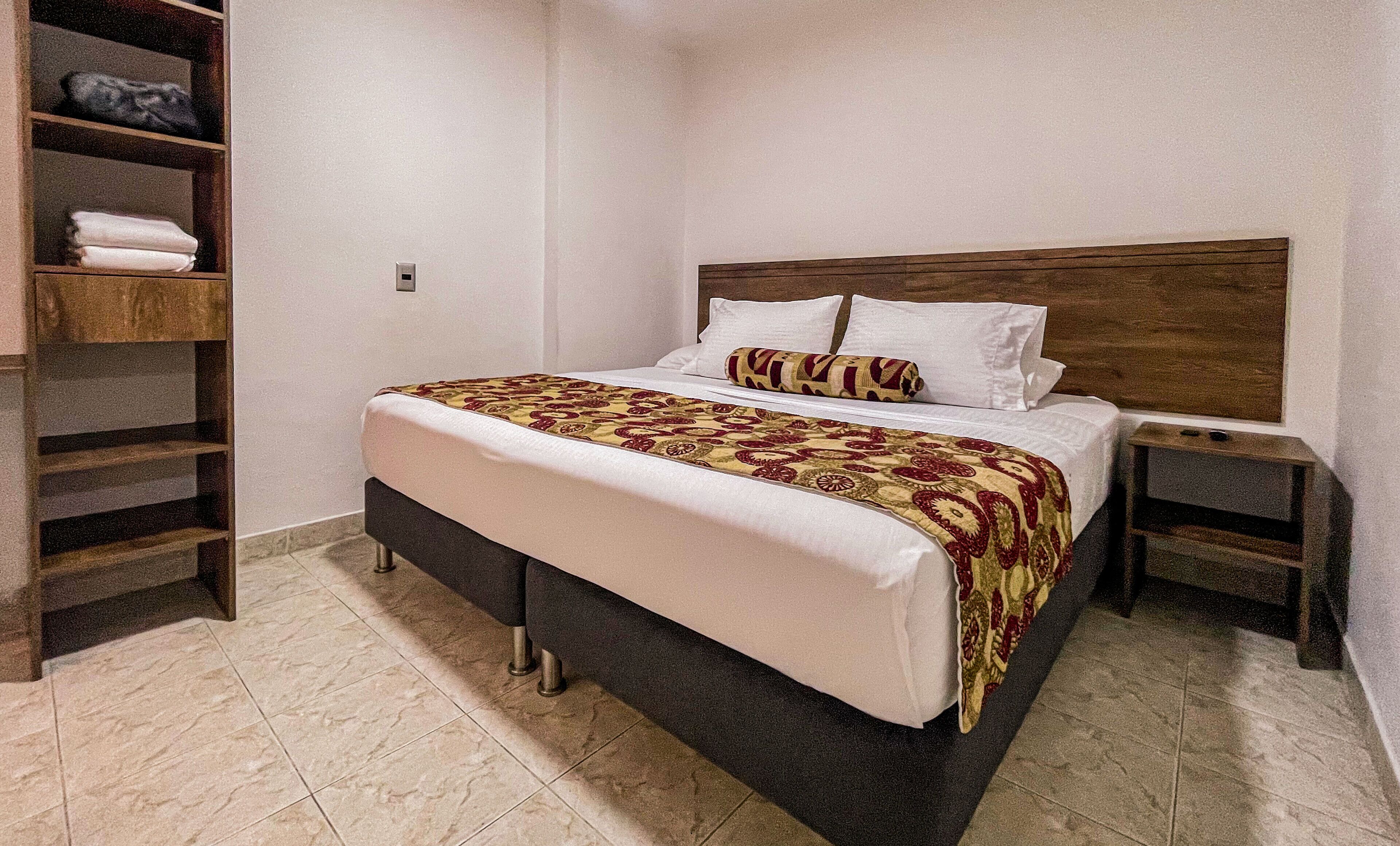 A neatly made bed with a patterned bedspread, a wooden headboard, and a nightstand with a lamp.