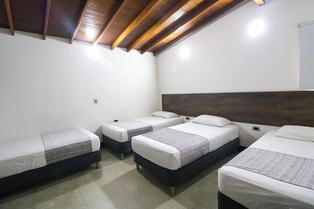 Ein Hotelzimmer mit vier Einzelbetten, Holzbalkendecke, weißen Wänden und Fliesenboden.