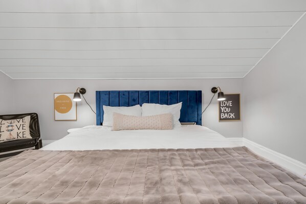A bedroom with a blue headboard, white bedding, a fluffy beige rug, and two wall-mounted lamps.