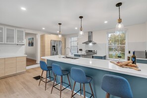 A modern kitchen with a central island, bar stools, stainless steel appliances, and pendant lighting.