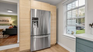 Une cuisine moderne dotée d’un réfrigérateur en acier inoxydable, de meubles en bois et d’une fenêtre donnant sur l’extérieur.