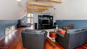 A spacious living room with a high ceiling, wooden beams, a black entertainment unit, and a large window. - Luxury Barn with Best View in the Cuyahoga National Park.   (Peninsula)