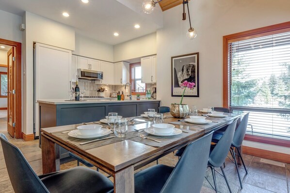 Una cocina moderna con armarios blancos, una isla central y un comedor con una mesa larga preparada para seis personas.