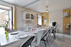 A dining area with a long table set for six, white chairs, a vase with a flower, and a white cabinet with glass doors.