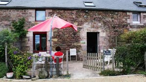 Un bâtiment en pierre avec un parasol rouge, une clôture en bois et une enseigne.