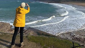 Une personne portant un blouson jaune prend une photo de l’océan.