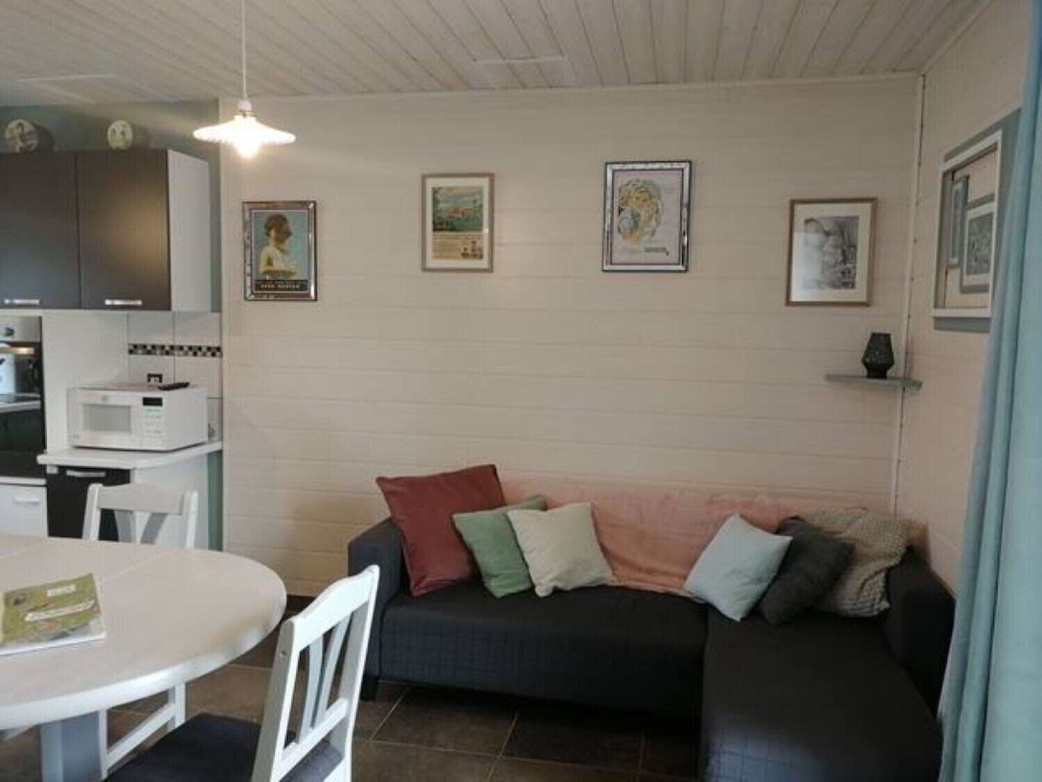 A cozy living area with a dark sofa, a white table, and a microwave. There are framed pictures on the wall and a clock above the sofa.