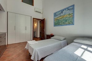 Quarto com duas camas, um guarda-roupa, um quadro e um banheiro visível por uma porta aberta.
