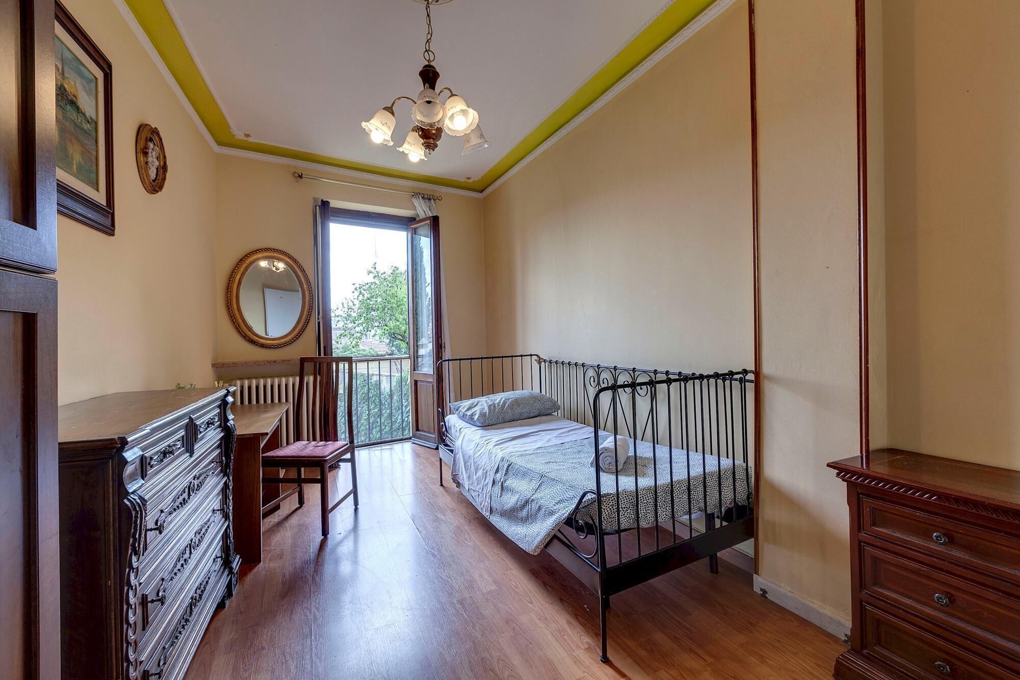 Un dormitorio con cama, cómoda, silla, espejo y ventana con vistas a la vegetación.
