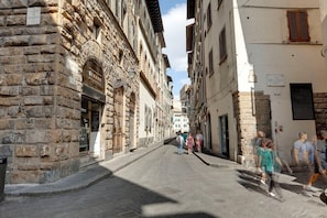 A narrow street lined with historic stone buildings, some with visible shop fronts and signage.
