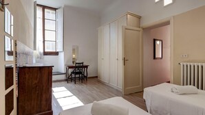 A bedroom with two beds, a desk, a wardrobe, and a radiator. - Neri 23 in Firenze With 3 Bedrooms and 2 Bathrooms (Florence)