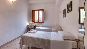 A small, clean room with two beds, a desk, and a window with wooden shutters.