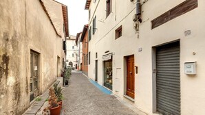 A narrow cobblestone street flanked by buildings with closed shutters and a few open windows.