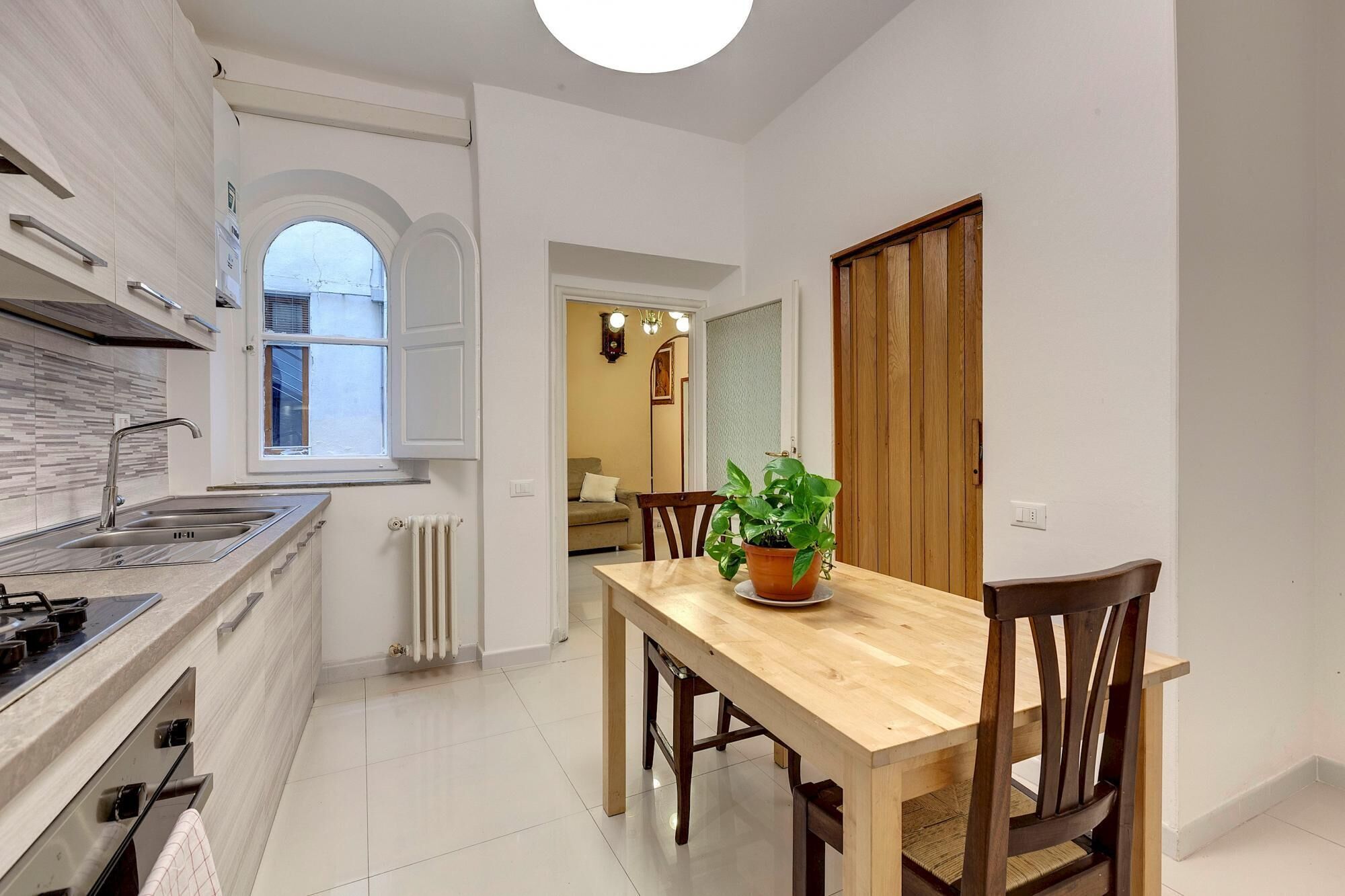 Une cuisine moderne avec un coin repas, comprenant une table et des chaises en bois, une plante en pot et une vue sur le salon adjacent.