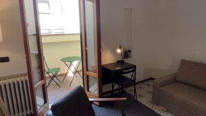 A living room with a sofa, a chair, a small table, and a sliding glass door leading to an outdoor area with a table and chairs. - Agnolo 73 IV in Firenze (Florence)