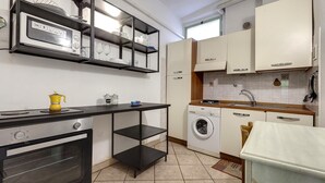 A modern kitchen with a built-in oven, microwave, and washing machine. There are black shelves above the counter and a small table with a yellow kettle. - Sapiti 2 G in Firenze (Florence)
